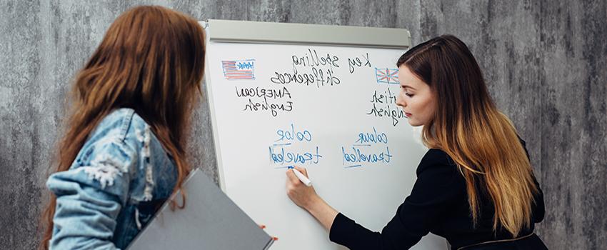 Woman writing on white board while another woman looks on,.